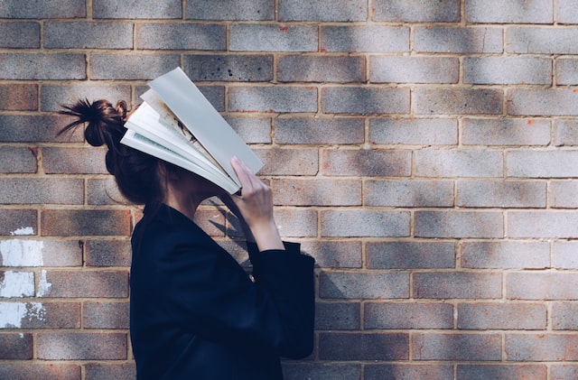 Una chica tapándose el rostro con un libro