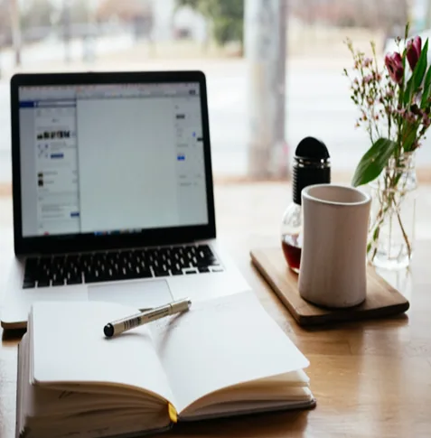 Un portátil, un cuaderno y una taza sobre una mesa